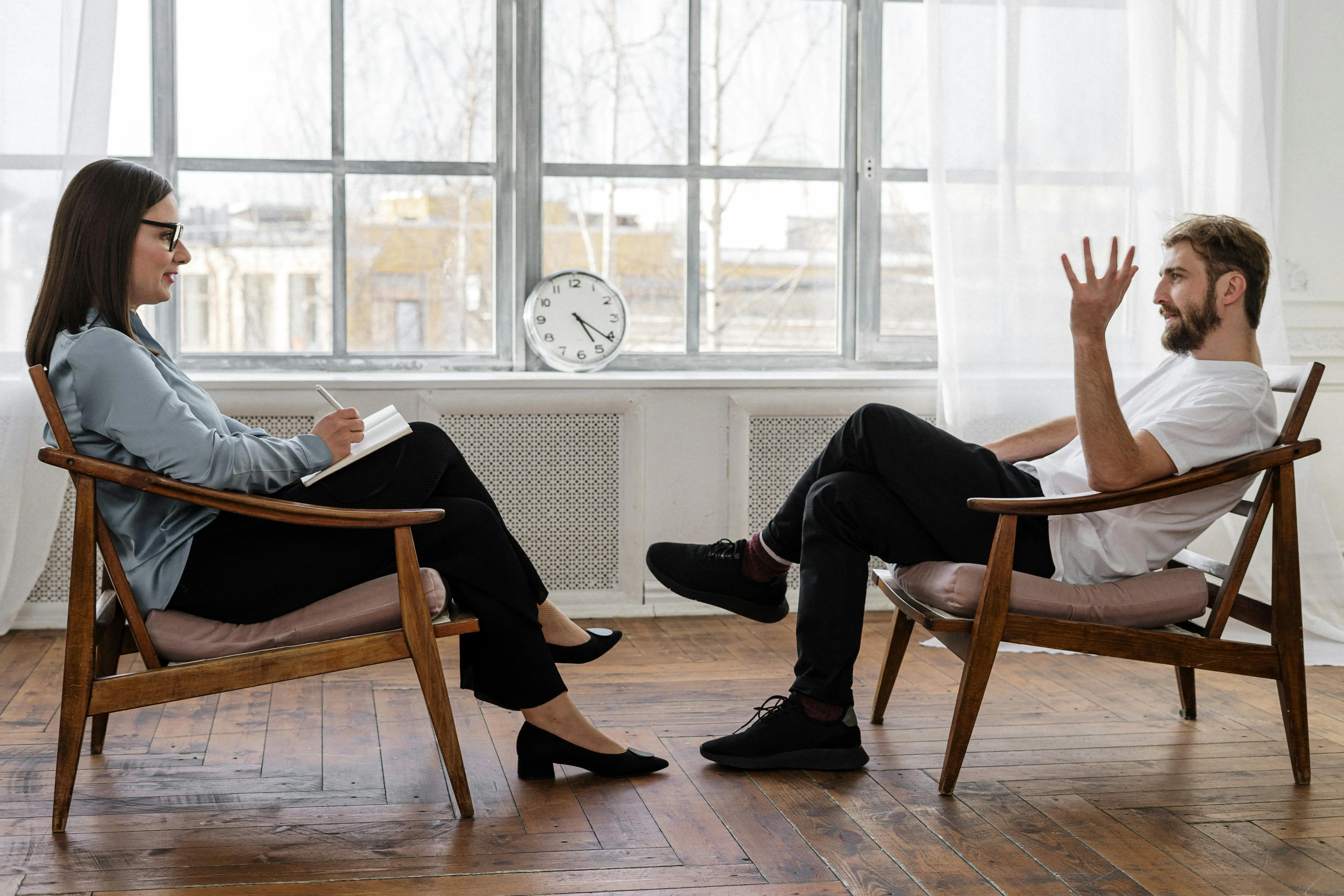 a man and woman sitting in chairs having a discussion regarding treatment programs